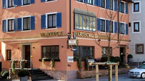 Un hotel con fachada color melocotón, contraventanas azules y un letrero que dice "Warteck Hotel".