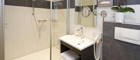 A modern bathroom with a glass-enclosed shower, a white sink, a mirror, a towel rack, and a potted orchid.