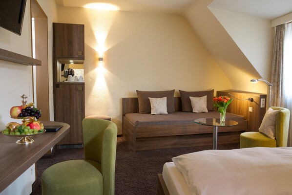 Habitación de hotel con sofá, cama, escritorio con frutero, silla y mesita con un florero.