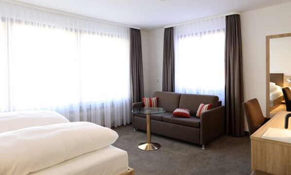 Una habitación de hotel con cama, sofá, una mesita redonda y un escritorio con lámpara.