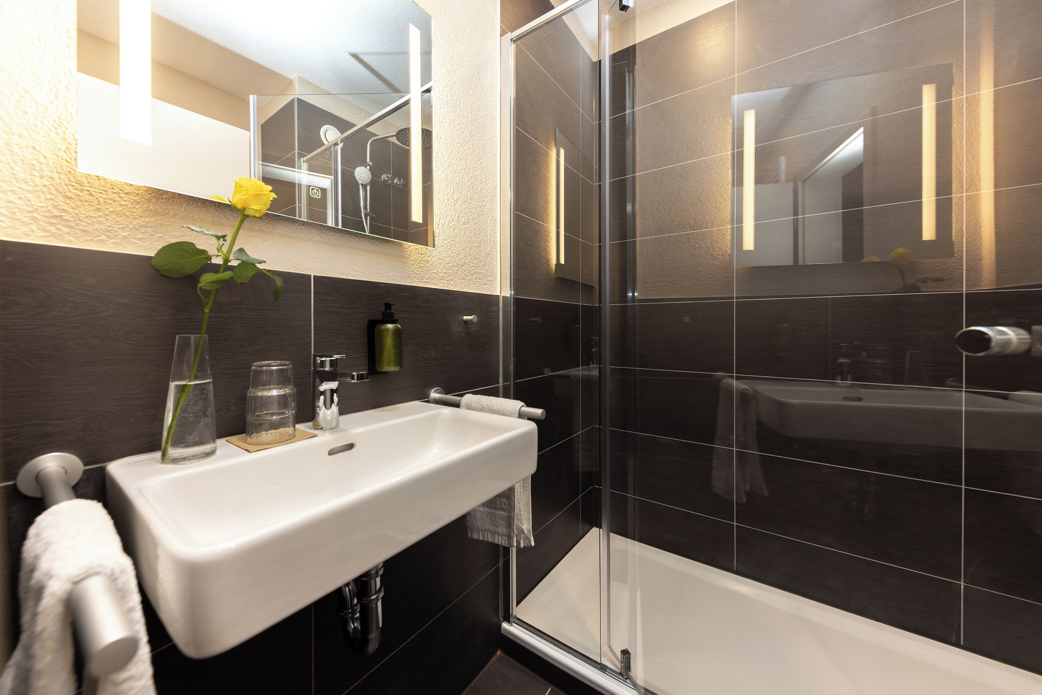 Ein modernes Badezimmer mit einem weißen Waschbecken, einer Duschkabine aus Glas und einem Spiegel über dem Waschbecken.