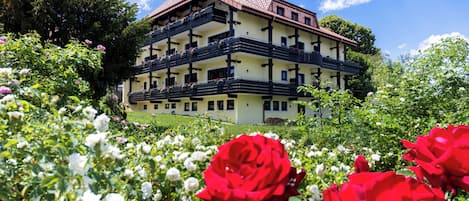 Um edifício com várias andares e varandas, cercado por vegetação exuberante e plantas floridas.