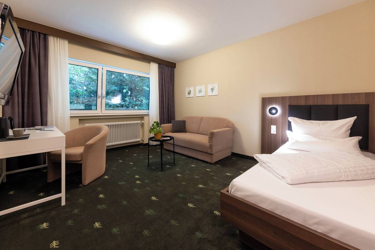 A hotel room with a bed, a sofa, a desk, and a window with curtains.