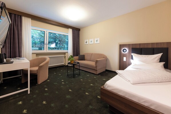 Una habitación de hotel con cama, sofá, escritorio y ventana con cortinas.