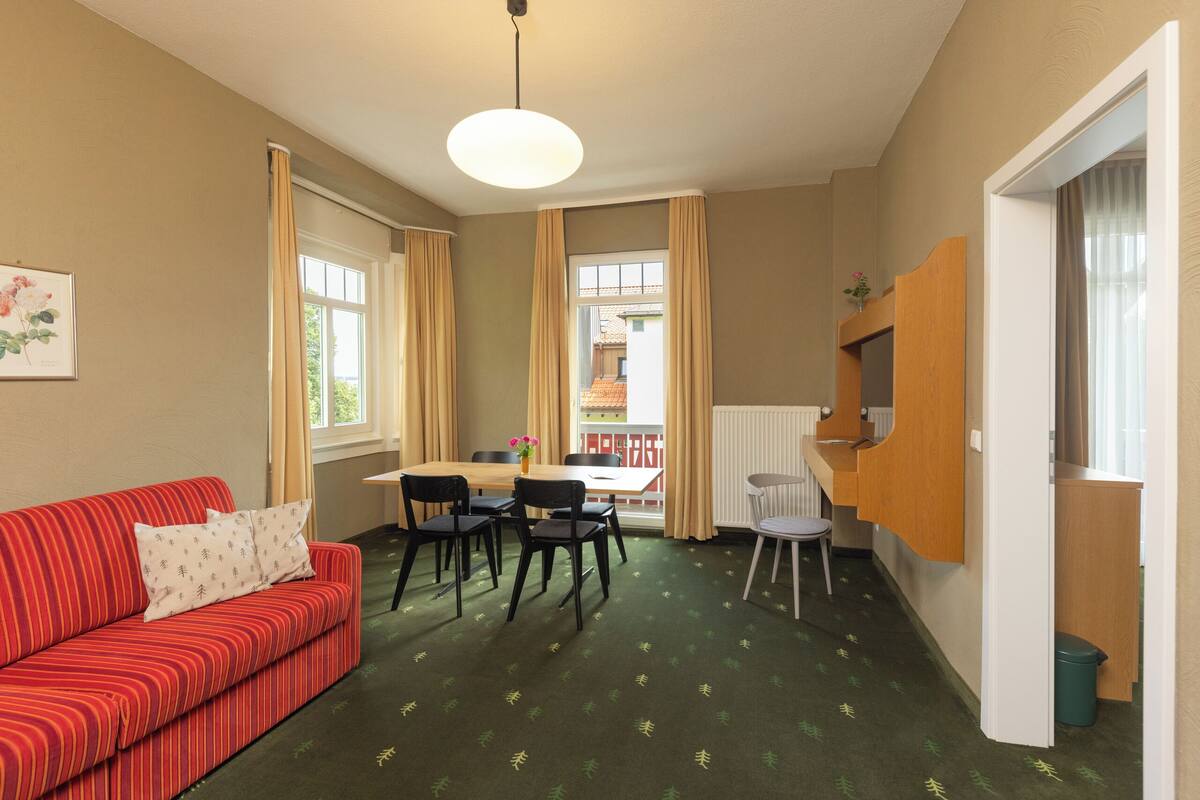 A room with a red-striped sofa, a dining table with chairs, a hanging light fixture, and a view of a building outside.