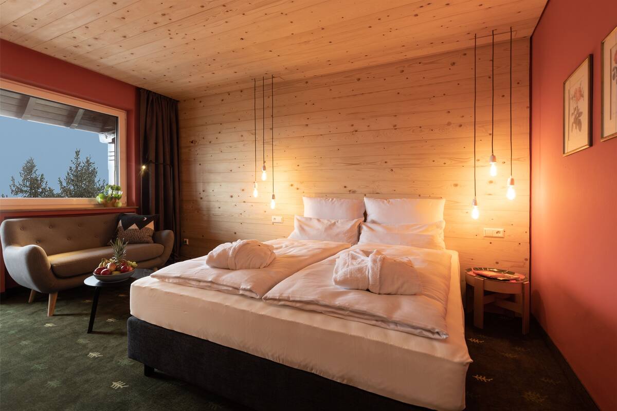 A hotel room with a wooden ceiling, a bed with white linens, a small table with fruit, a chair, and a nightstand.