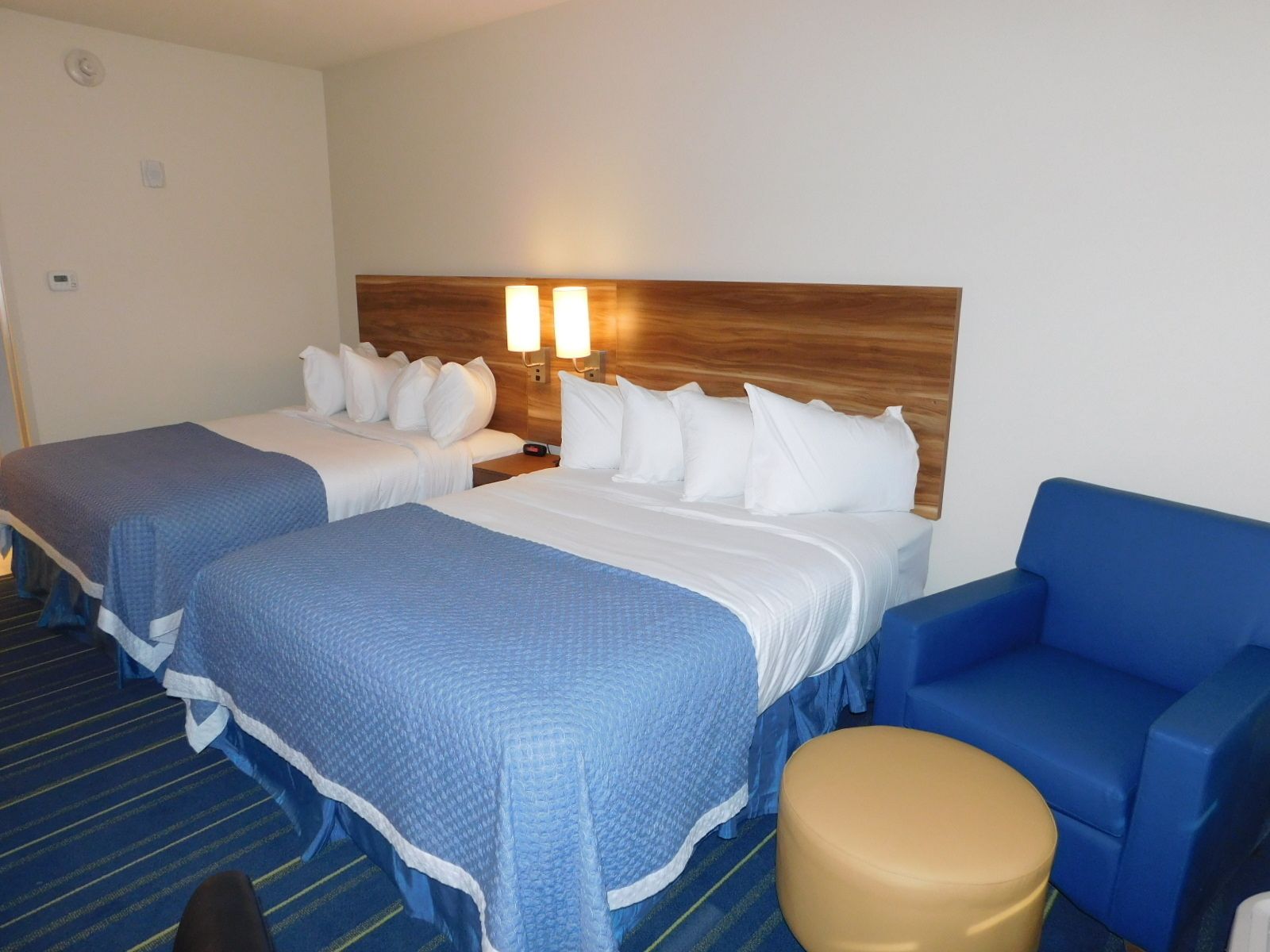 Una habitación de hotel con dos camas, un cabecero de madera, un sofá azul y un taburete pequeño.
