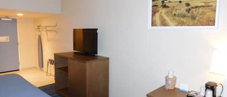 A hotel room with a bed, a desk with a lamp, a television, and a painting of a landscape.