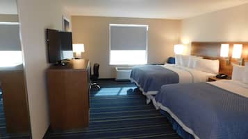 Une chambre d’hôtel avec deux lits, un bureau avec une télévision, une chaise et une fenêtre avec des stores.