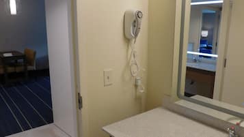 Een hotelbadkamer met een wastafel, spiegel en een haardroger aan de muur.