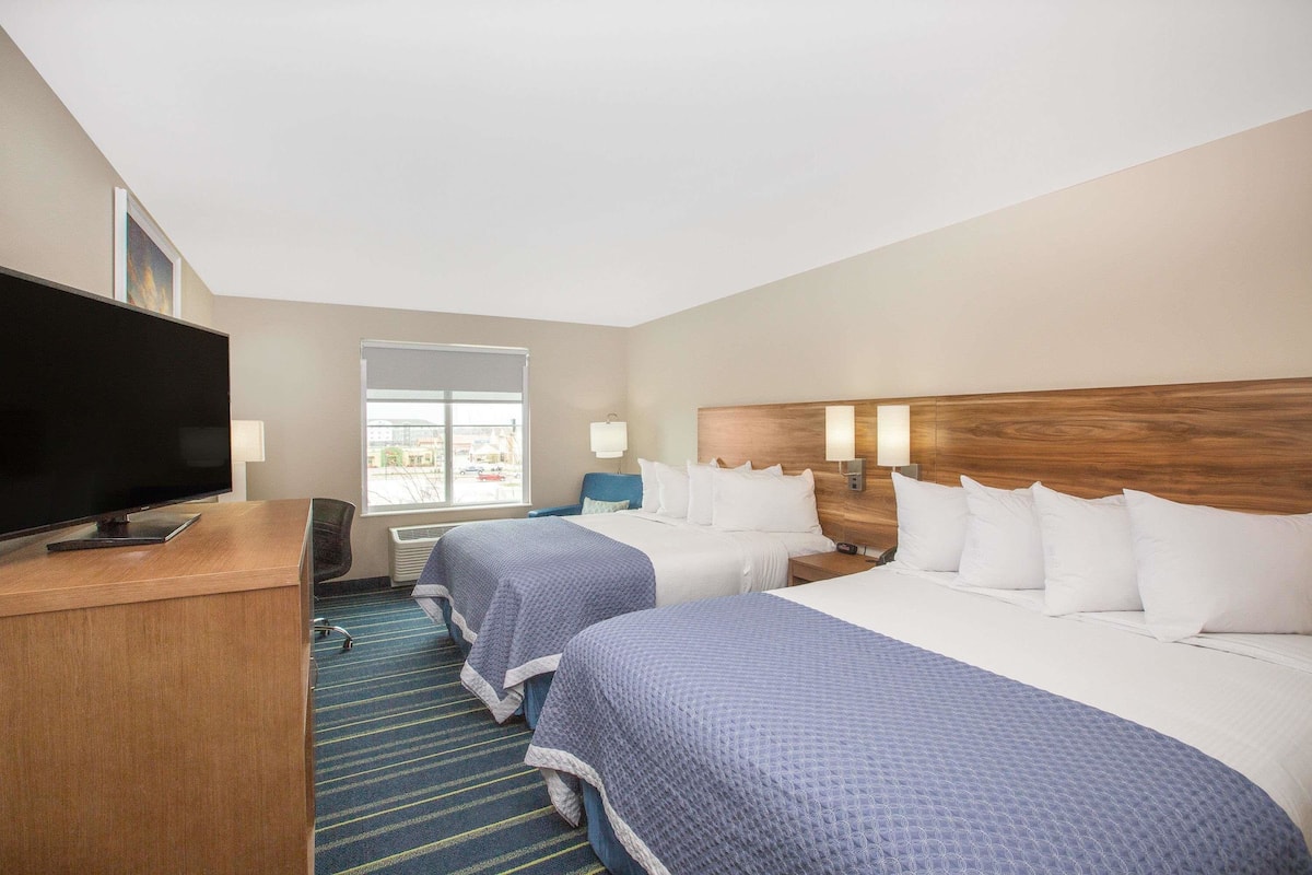 A hotel room with two beds, a desk with a flat-screen TV, a window, and a view of the outside.