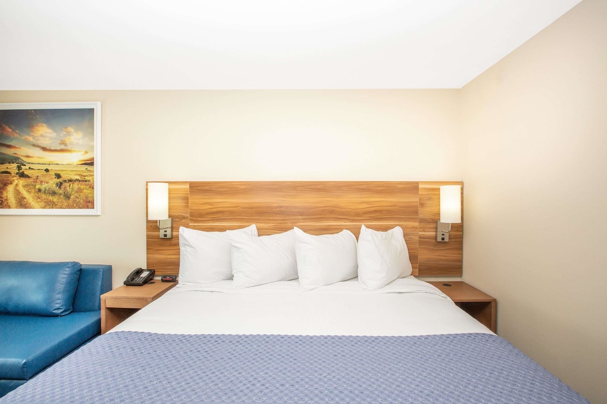 A hotel room with a large bed, two bedside tables, a blue sofa, and a painting on the wall.