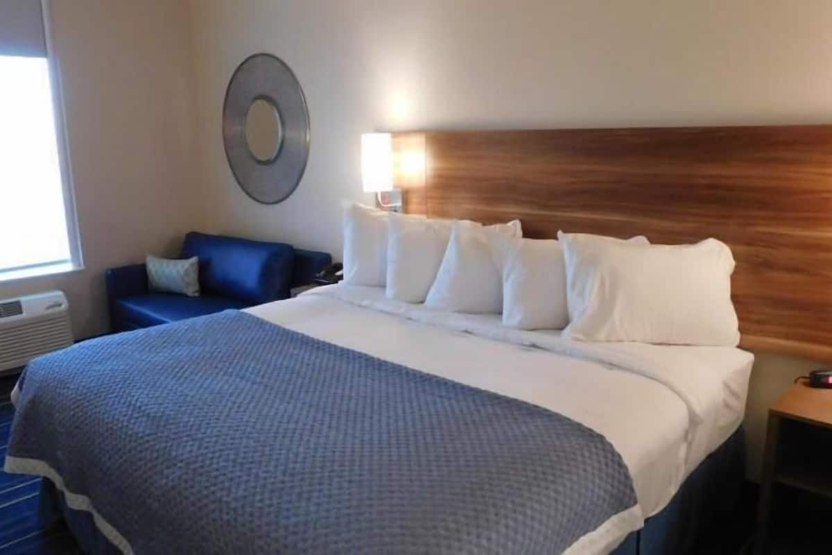 A hotel room with a large bed, a blue sofa, a round wall decoration, and a bedside table with a clock.
