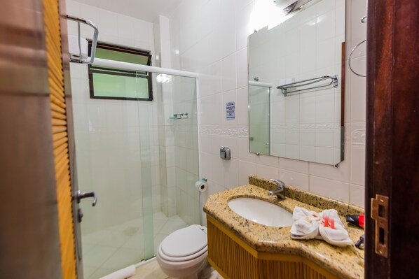 A bathroom with a glass shower enclosure, a toilet, a sink with a granite countertop, and a mirror above the sink.