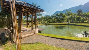 A pavilion with a tiled roof overlooking a pond, surrounded by palm trees and mountains. - Estância Ribeirão Grande (Jaragua do Sul)