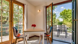 Un coin repas avec une table et deux chaises, un vase rempli de fleurs rouges et une vue sur une terrasse extérieure avec des chaises et des tables.
