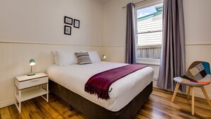 Une chambre à coucher avec un lit, une table de chevet avec une lampe, une chaise et une fenêtre avec des rideaux.