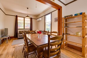 A dining area with a wooden table, chairs, and a vase of red flowers. There is a bookshelf with books and a television on a stand.
