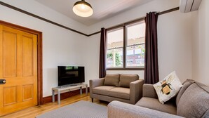 Un salon avec un canapé, un téléviseur, une porte en bois et une fenêtre avec des rideaux.