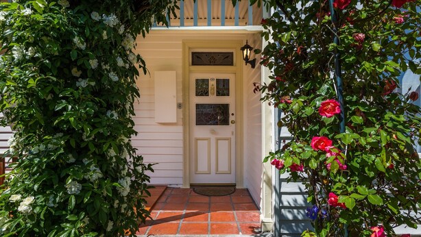 Une maison avec une porte blanche, un petit porche et un jardin où poussent différentes sortes de fleurs.