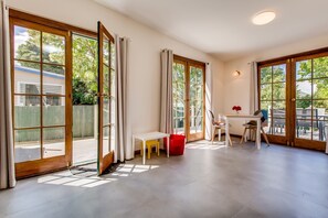 A spacious room with large sliding glass doors, a white table with chairs, and a red bucket.
