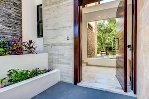 Enter a serene space with a clean design, featuring a textured wall, wooden door frame, and lush greenery.