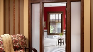 A room with a patterned armchair, a wooden door, and a view into a bathroom with a bathtub and a window. - The Buckingham Inn (Madison)