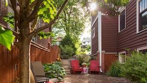 A backyard with a wooden fence, a tree, and a red Adirondack chair. - The Buckingham Inn (Madison)