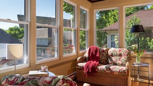 A cozy room with a wicker sofa, a table with a lamp, and large windows offering a view of the outside. - The Buckingham Inn (Madison)