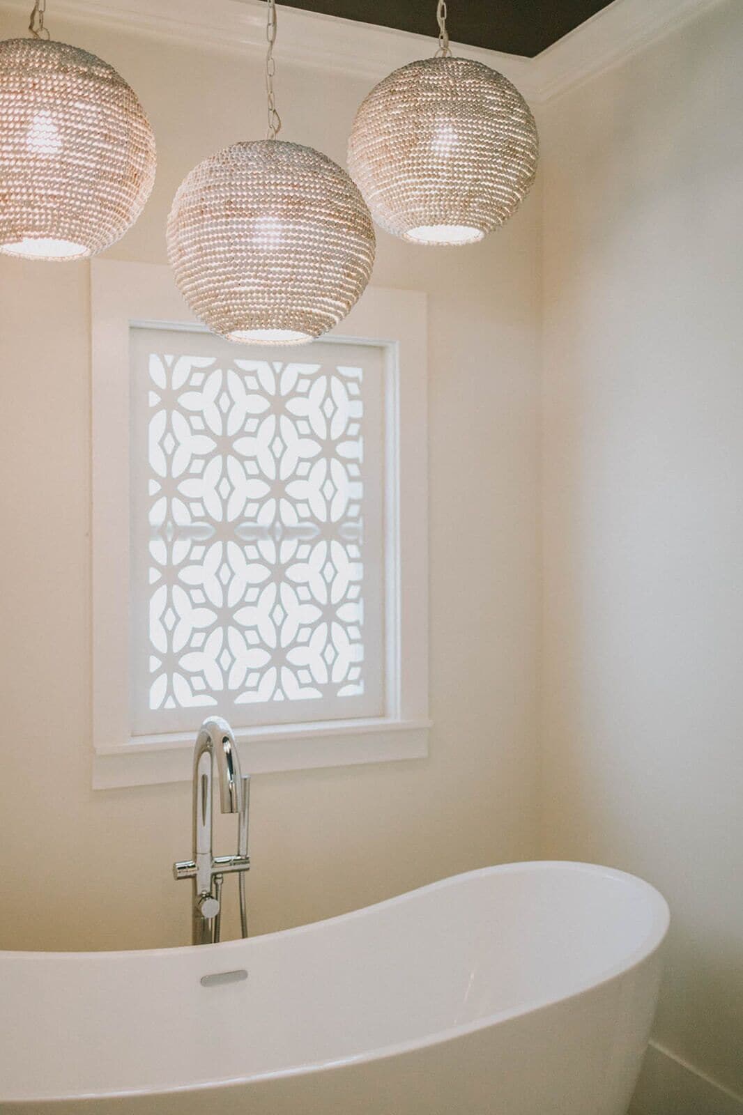 Un baño con una bañera independiente, un ventanal decorativo con diseño geométrico y tres lámparas colgantes.