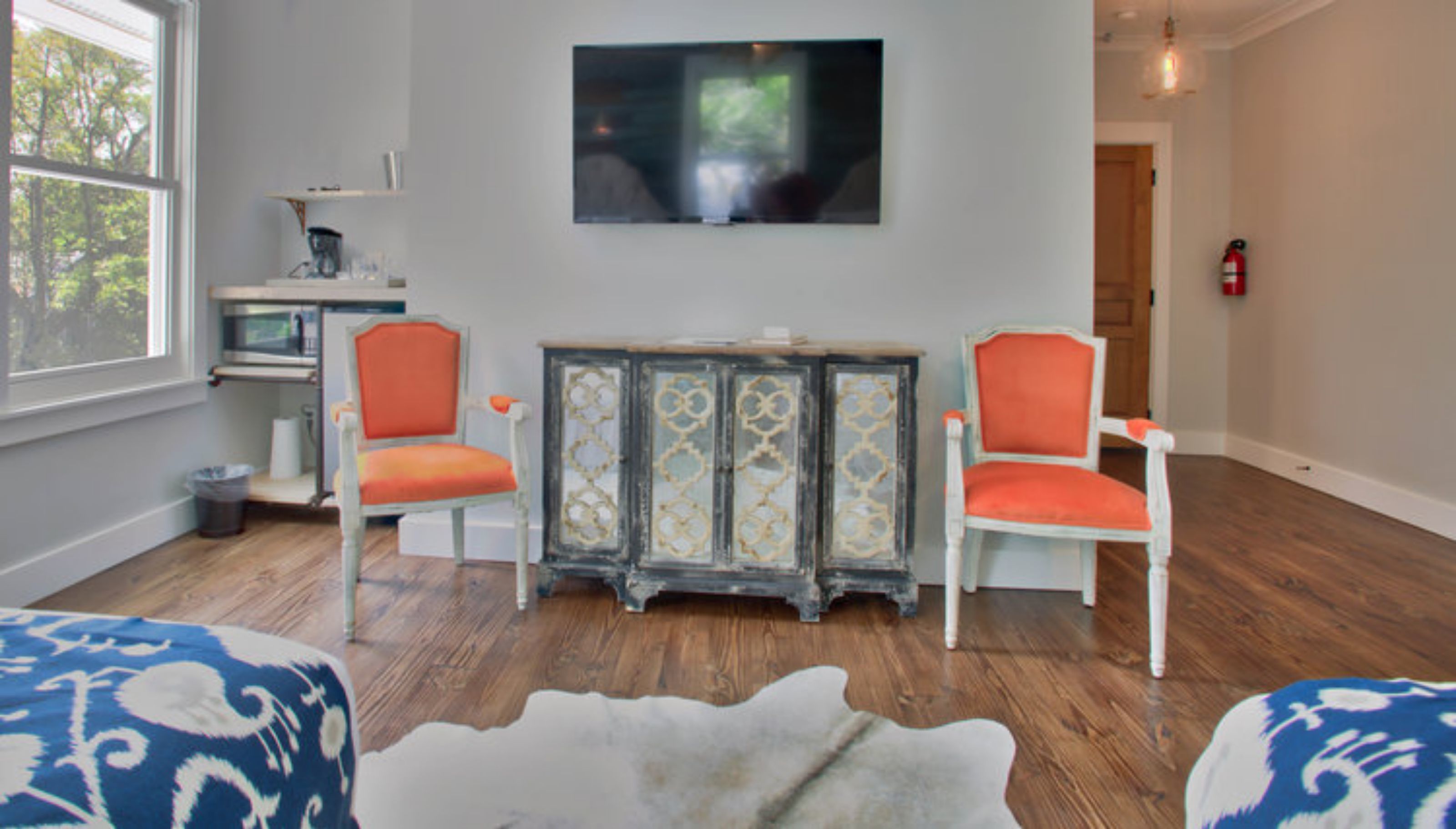 A living room with two orange chairs, a white sofa, and a wooden floor.