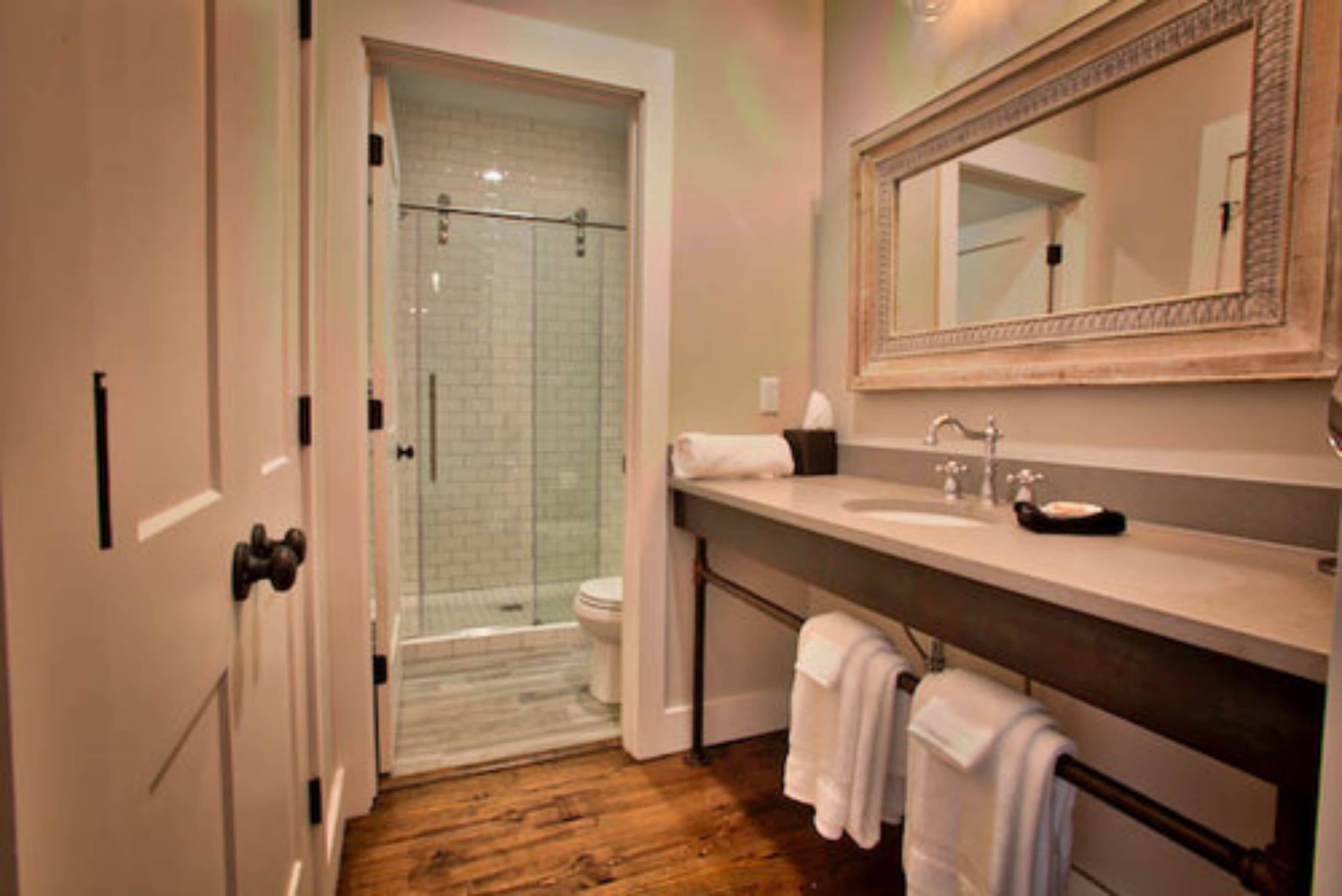 Une salle de bain avec une douche à parois de verre, un lavabo avec un miroir et un revêtement de sol en bois.