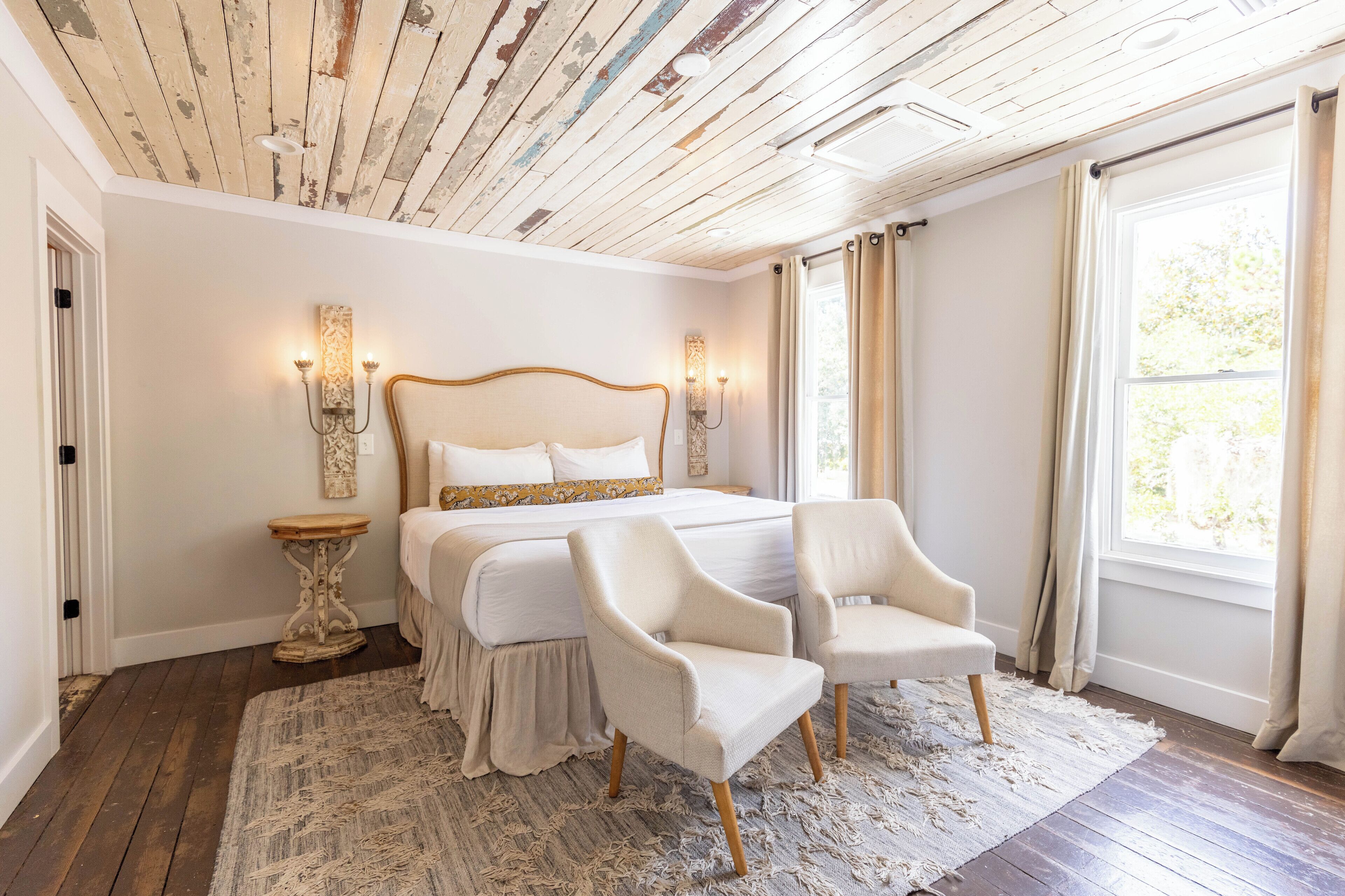 A bedroom with a large bed, two chairs, a nightstand, and a wooden ceiling.