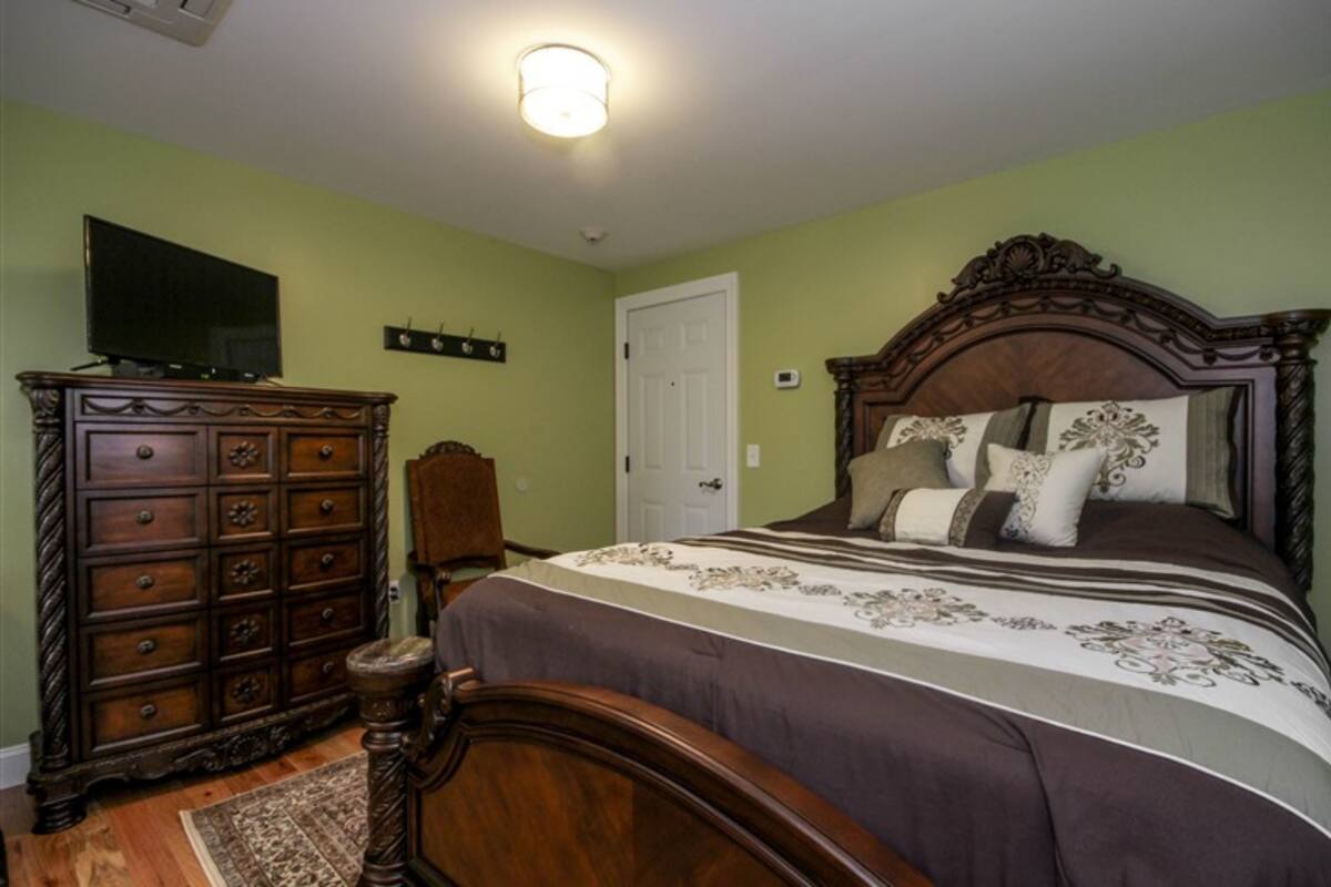 Une chambre à coucher avec un lit en bois, une commode et un téléviseur posé sur un meuble.