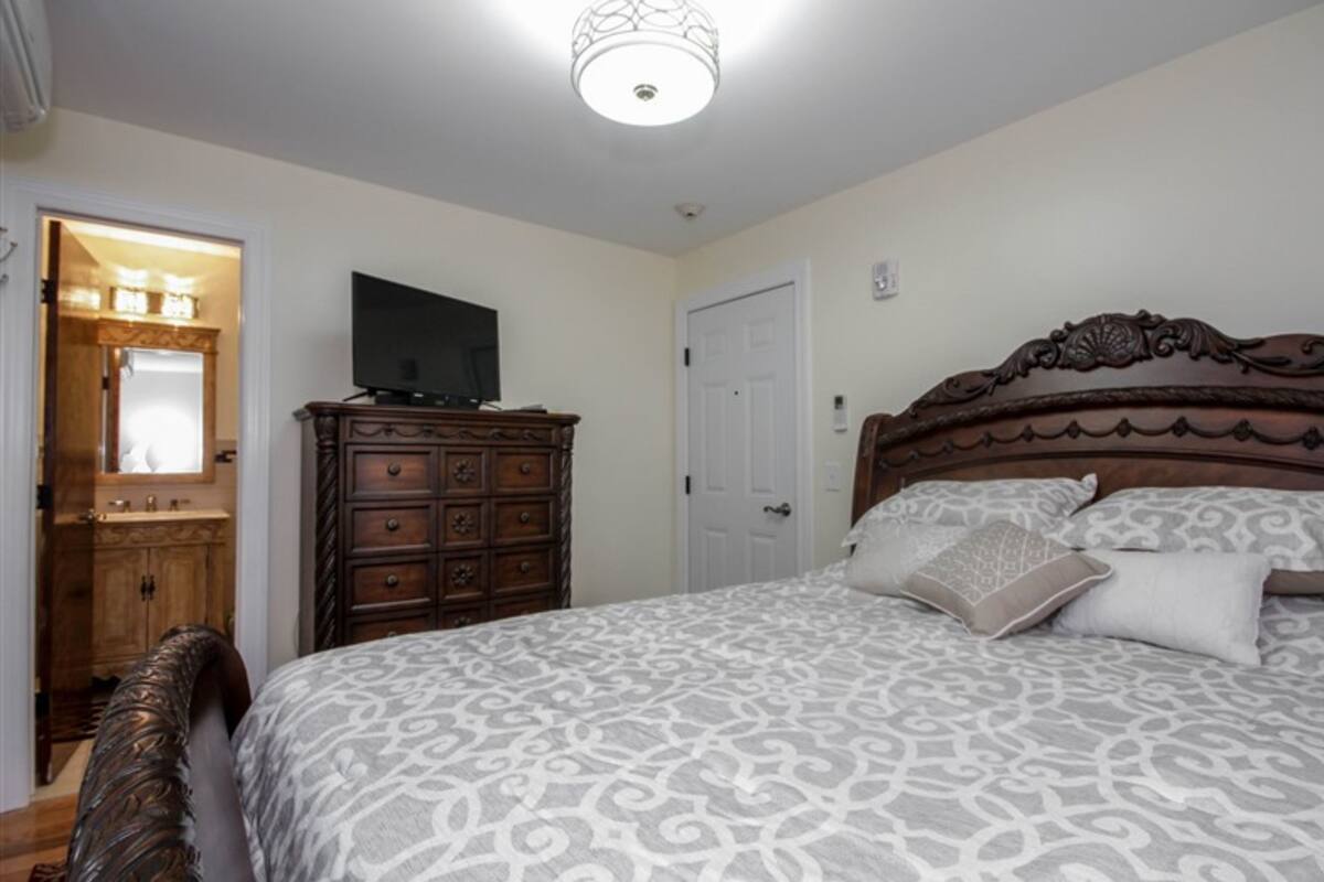 Une chambre à coucher avec un grand lit, une commode en bois et un téléviseur posé sur le dessus.