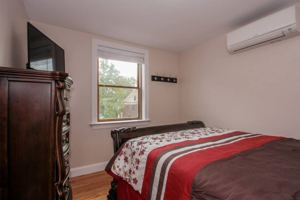 Une chambre à coucher comprenant un lit, une commode, une fenêtre et un appareil de climatisation.