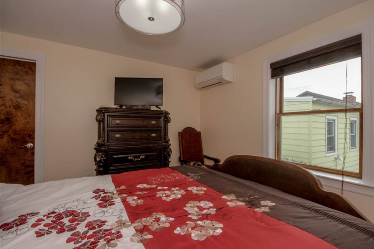 Une chambre à coucher comprenant un lit, une commode, une chaise et une fenêtre donnant sur une maison.
