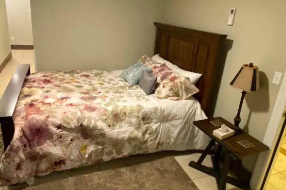 Une chambre à coucher avec une couvre-lit à motifs floraux, une tête de lit en bois et une table de chevet avec une lampe.