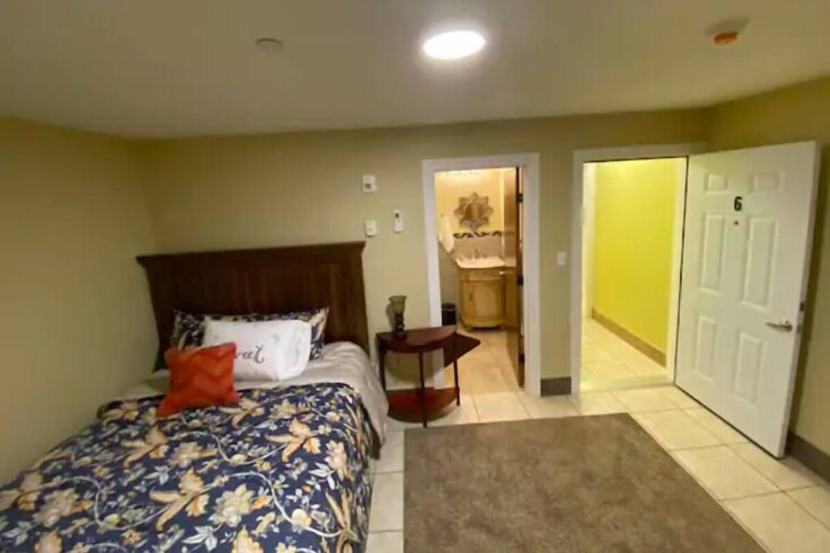 Une chambre à coucher avec un lit, une table de chevet, une porte et une salle de bain visible à travers une porte ouverte.