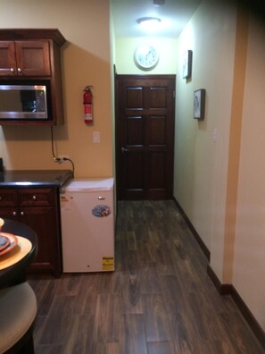 A kitchen with wooden cabinets, a microwave, a refrigerator, and a clock on the wall.