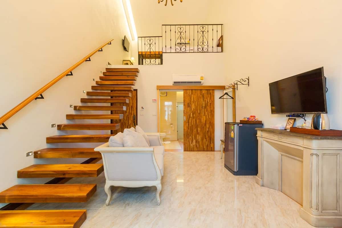 A modern interior with a wooden staircase, a white sofa, a kitchen area with a refrigerator, and a flat-screen TV.