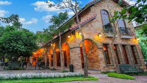 Un edificio de piedra con ventanas de arco y fachada de ladrillo, rodeado de un jardín con un sendero empedrado.