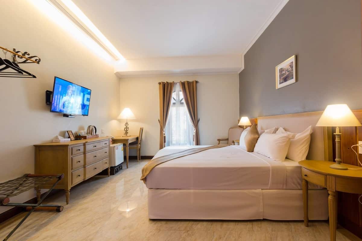 A hotel room with a bed, bedside tables, a desk, a chair, a television, and a window with curtains.