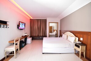 A hotel room with a bed, bedside table, chair, desk, TV, and curtains. - Fantasy Resort (Nakhon Sawan)
