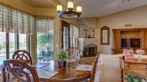 A dining area with a wooden table, chairs, and a chandelier. There is a fireplace with a stone mantle and a television on a wooden cabinet. - Great Location, Quiet, Beautiful and Comfortable Scottsdale Retreat (Scottsdale)