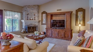 A living room with a stone fireplace, a television on a wooden cabinet, and a sofa with colorful cushions. - Great Location, Quiet, Beautiful and Comfortable Scottsdale Retreat (Scottsdale)