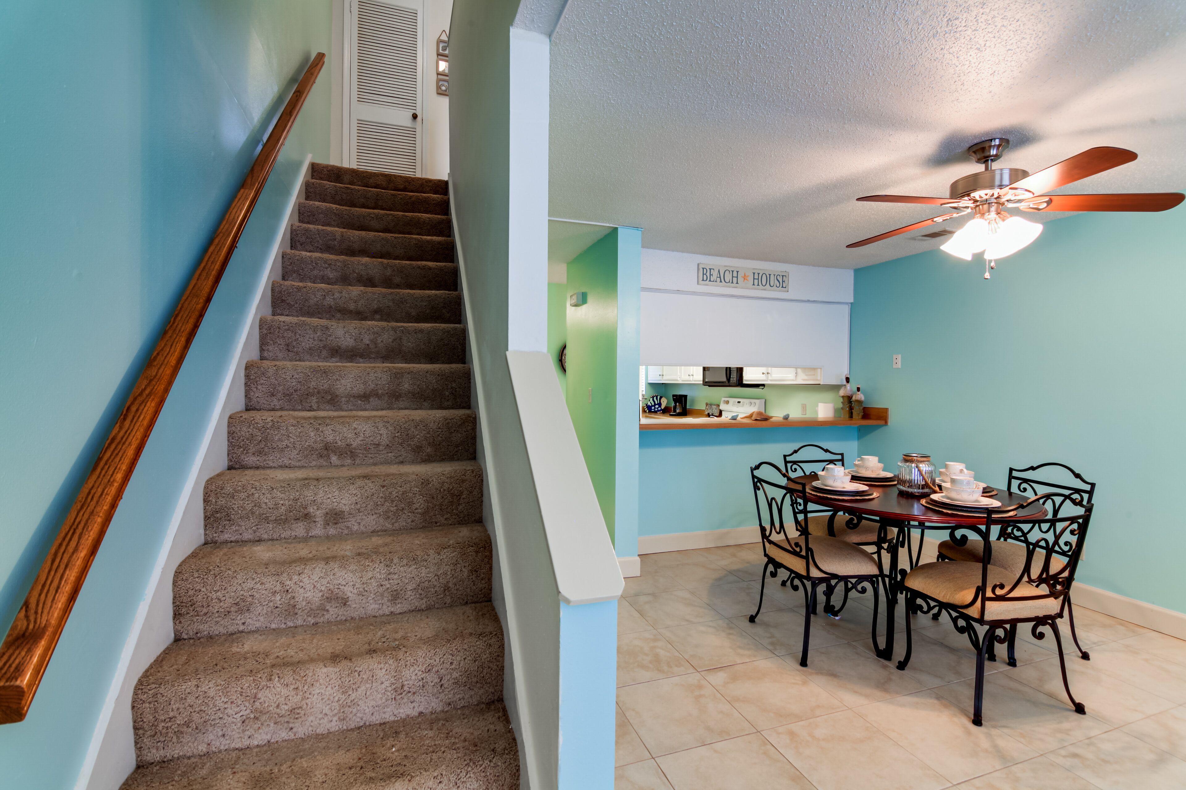 Un escalier avec une rampe en bois mène à un coin repas où une table est dressée pour quatre personnes.