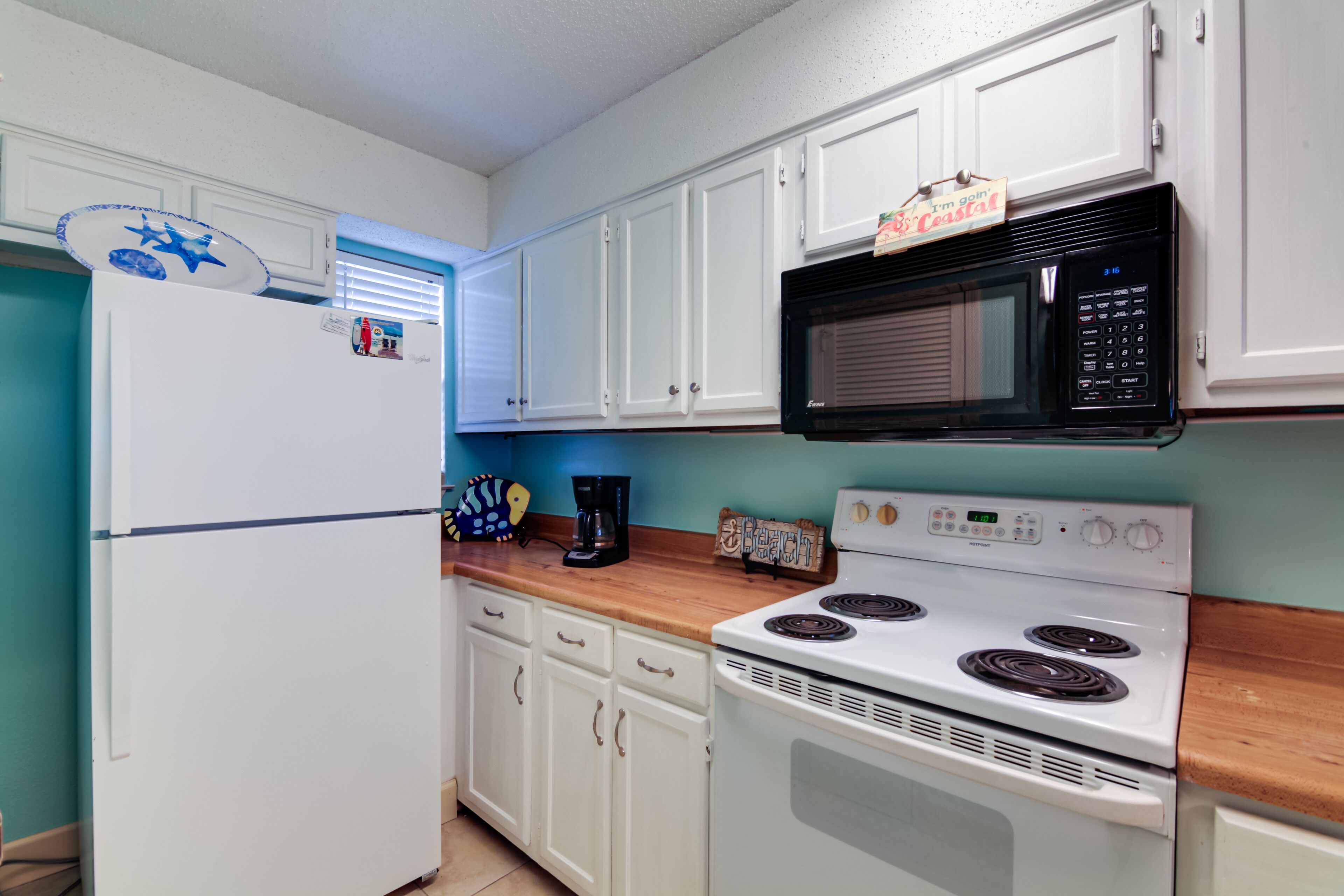 A kitchen with white cabinets, a black microwave, a white stove, and a refrigerator.
