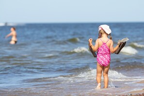A beach scene with a person in a pink swimsuit holding a surfboard. - Vacation in a historic Windmill on a large property near the Beaches, BREAKFAST (Karnice)