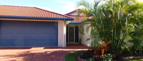 A house with a red-tiled roof, a garage, and a well-maintained lawn with tropical plants.